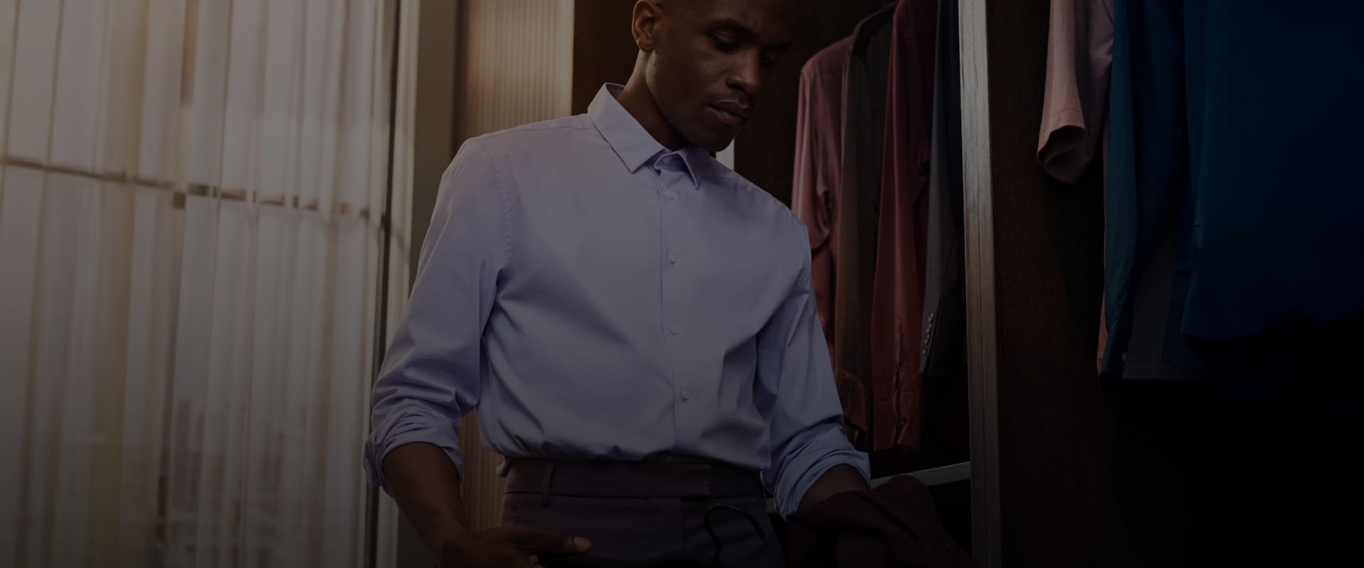 Mies sinisessä paidassa valikoi vaatteita vaatekaapista.